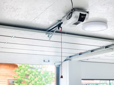Opening door and automatic garage door opener electric engine gear mounted on ceiling with emergency cord. Double place empty garage interior with rolling entrance gate