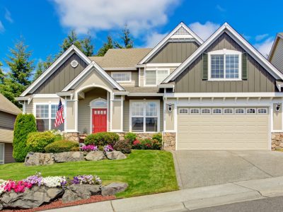 Grey house exterior with entrance porch and red door. Beautiful front yard landscape with vivid flower and stones